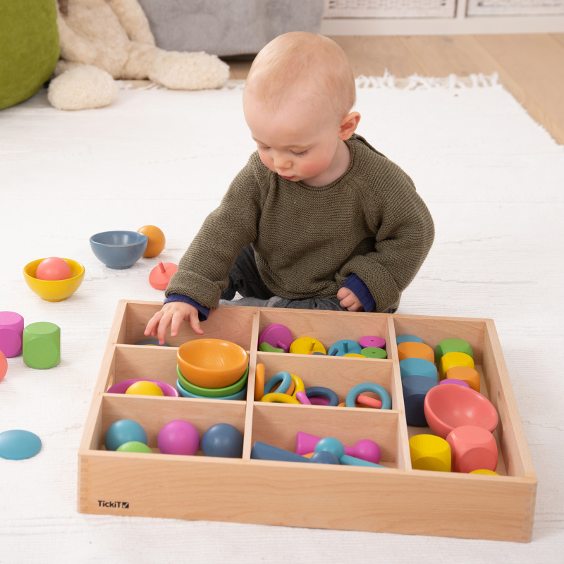 Child playing with colorful toys in a wooden sorting box on a white floor.