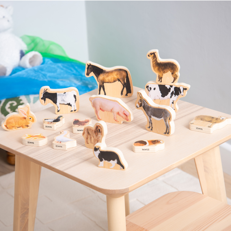 Set of wooden animal figurines on a light wooden table with a soft, blurred background.