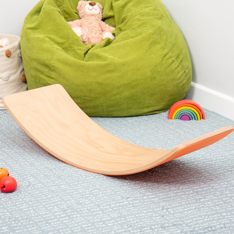 Wooden balance board on a textured surface with a green bean bag and toys in the background.