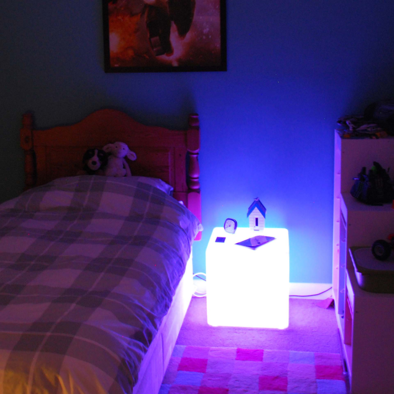 Bedroom with a night light emitting a blue glow, near a bed and dresser.