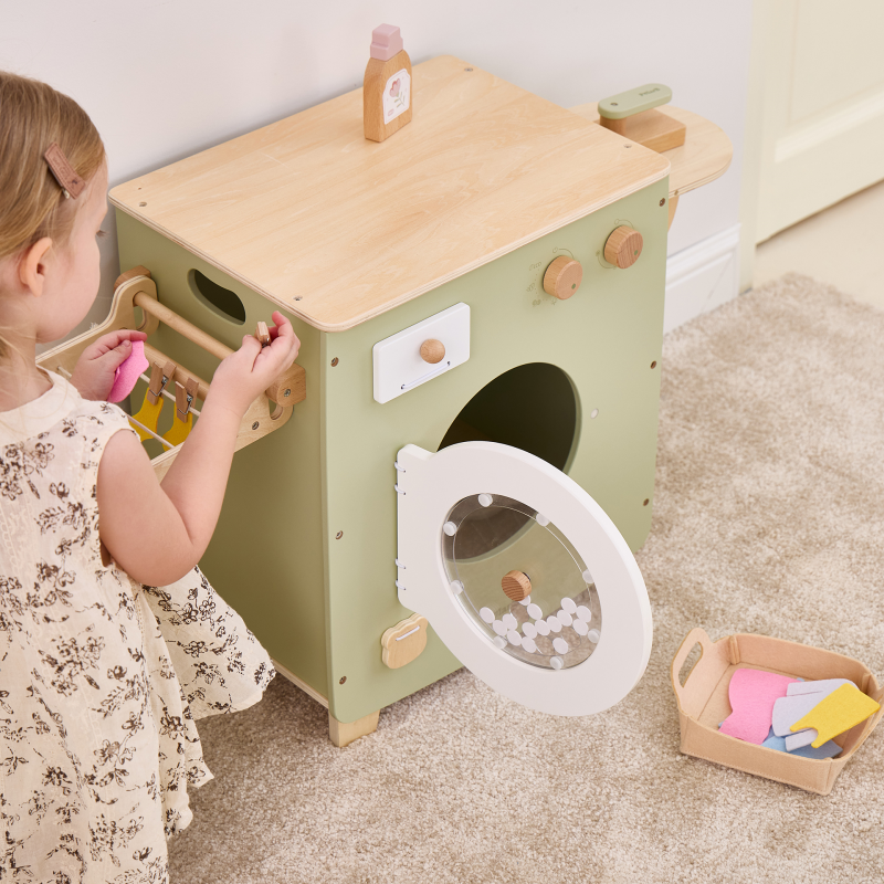 Child playing with a wooden toy washing machine on a carpeted floor.