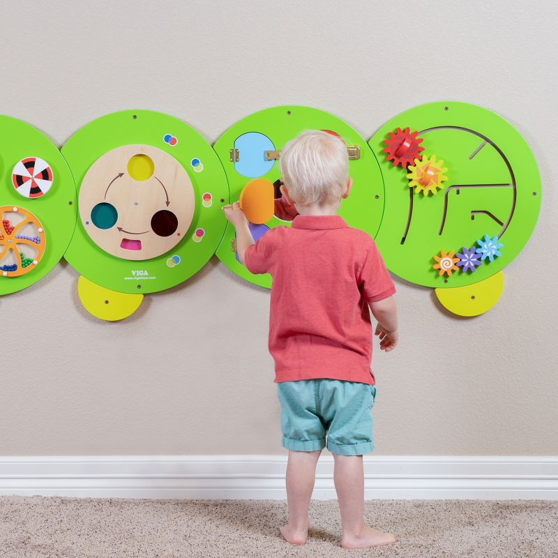 Child interacting with a colourful educational wall panel shaped like a caterpillar