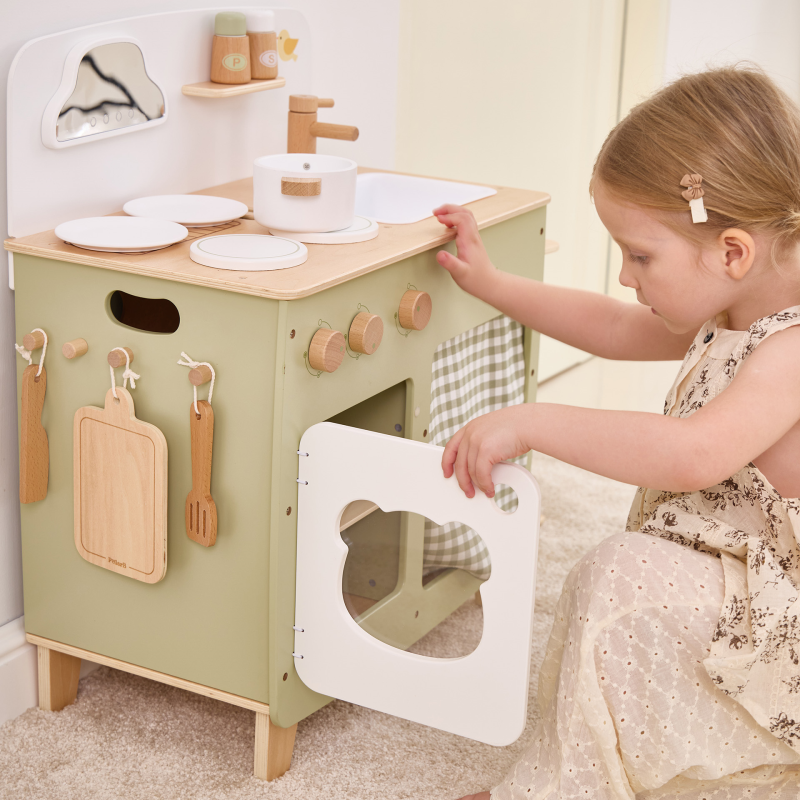 Child playing with a wooden play kitchen set in a home setting.