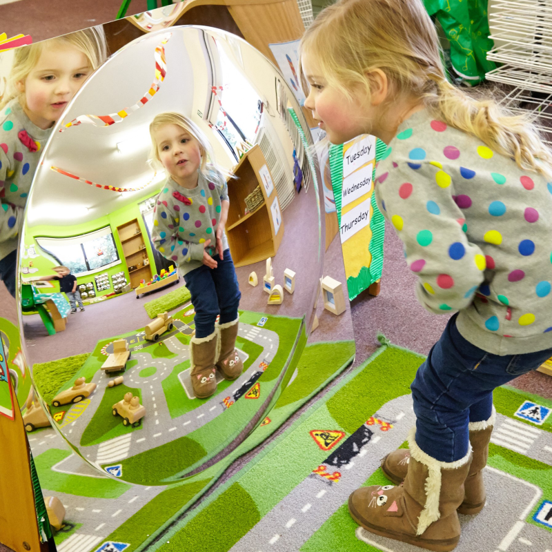 Child in a classroom setting looking at themselves in a mirror.
