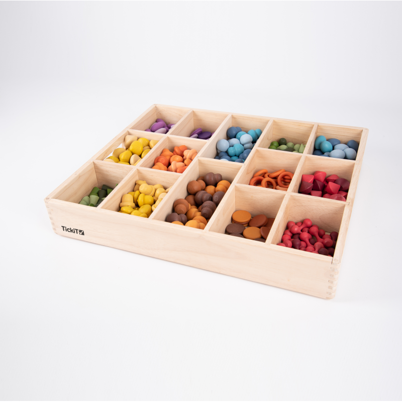 Wooden box with compartments filled with colourful loose parts on a white background