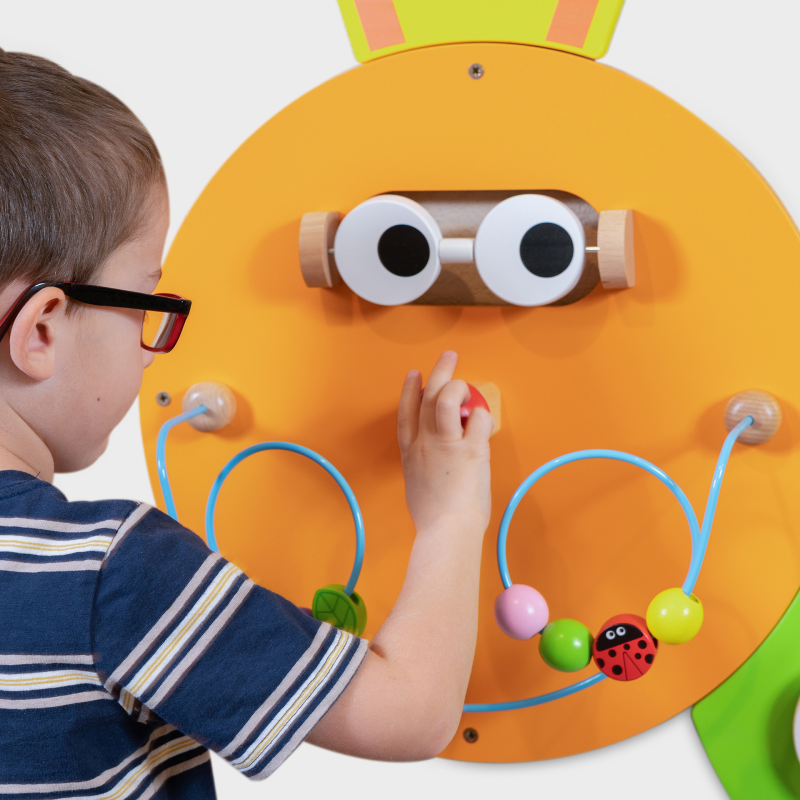 Child interacting with a colourful wall-mounted toy designed like a caterpillar.