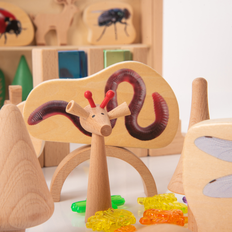 Wooden toy giraffe with a worm on a white surface, surrounded by other wooden toys.