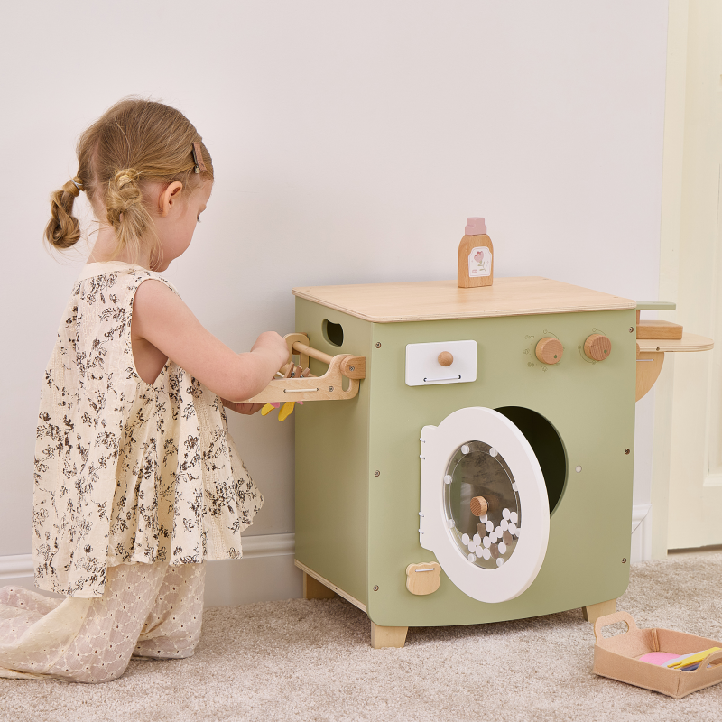 Child playing with a wooden toy washing machine in a room.