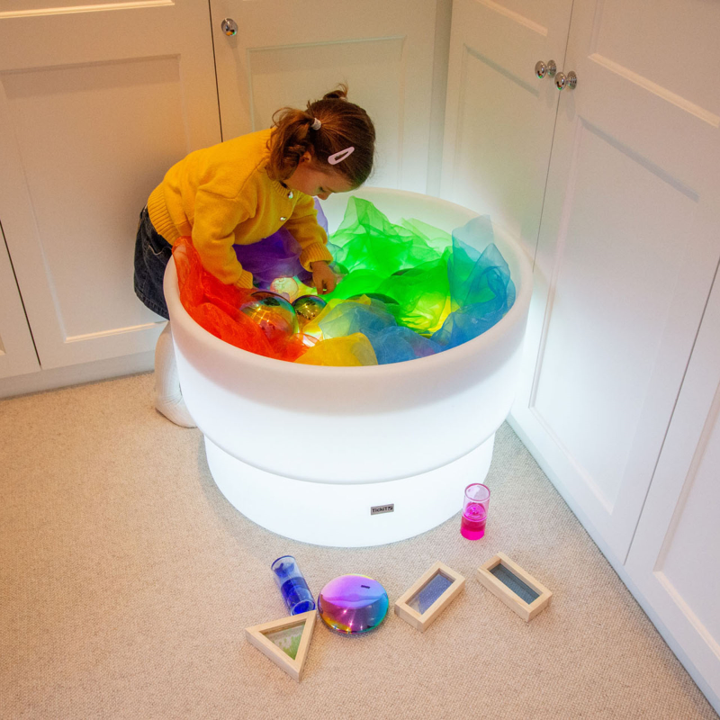 Child playing with colorful toys in a light-up table in a room with white cabinets.
