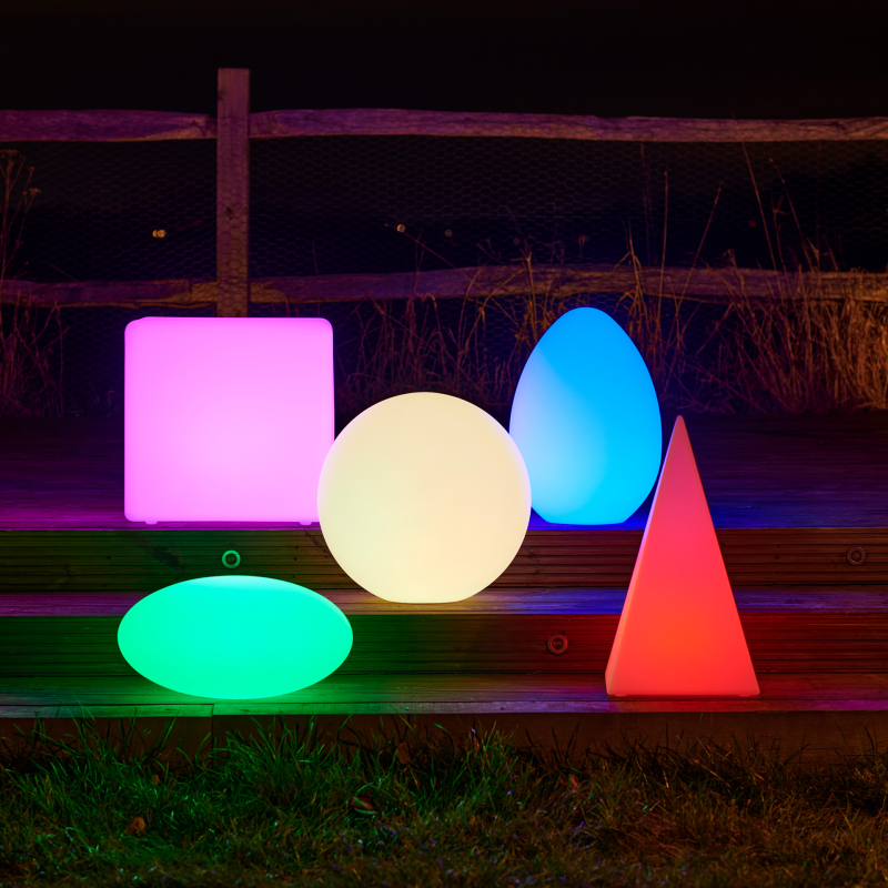Colorful LED lights shaped like a cube, sphere, cone, and egg on a wooden surface at night.
