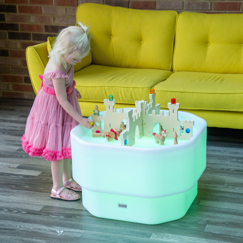 Child playing with a toy castle on a glowing green table in a room with a yellow couch.