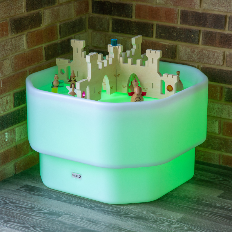 Wooden toy castle on a glowing green table against a brick wall.