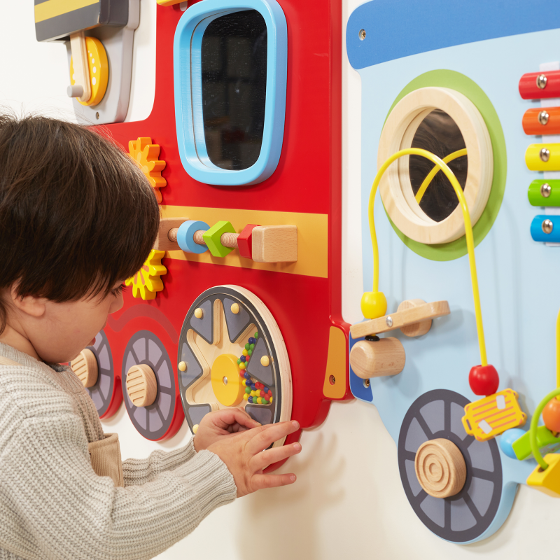 Child playing with a colorful educational wall panel featuring various interactive elements.