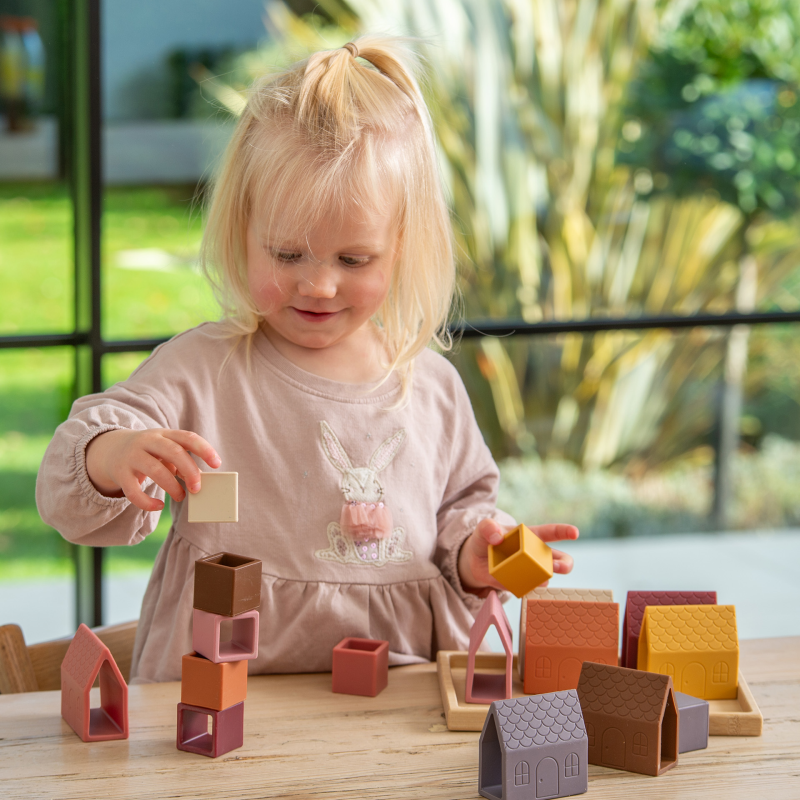 Child playing with colourful silicone building blocks on a wooden table outdoors.