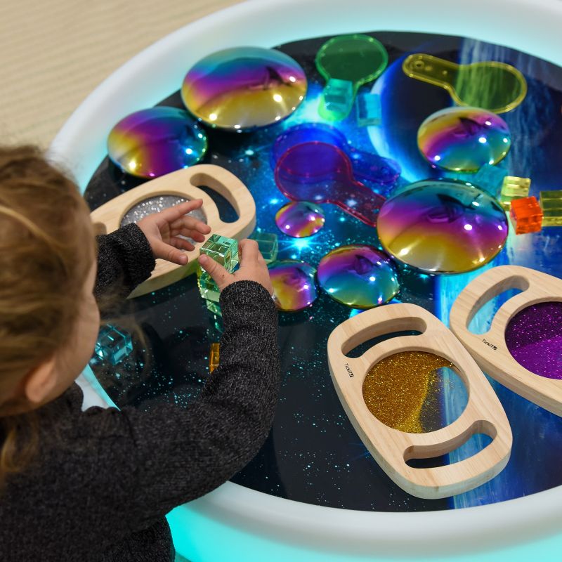 Child playing with colorful sensory toys in a glowing sensory light table.