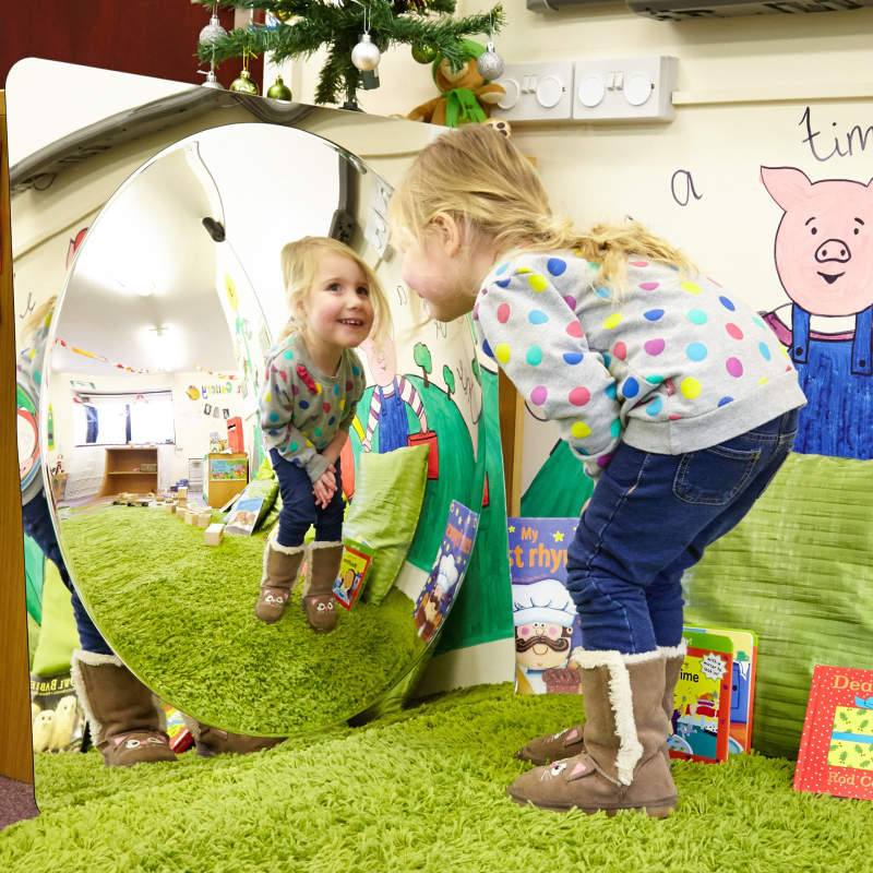 Child playing with a mirror in a classroom setting.
