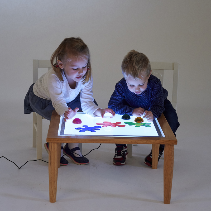 Two children playing with a light-up table on a plain background