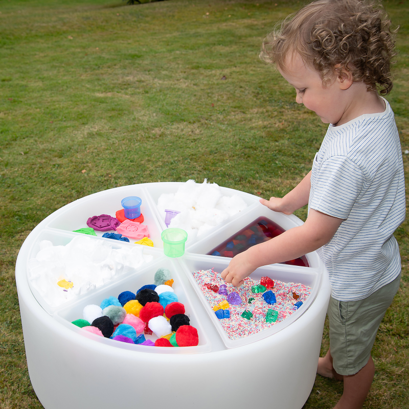 Child playing with a colorful sensory table outdoors on grass