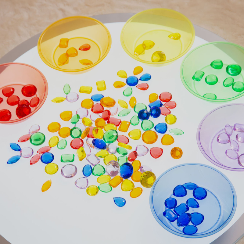 Colourful beads in various shapes and sizes on a light up round panel with colored containers.