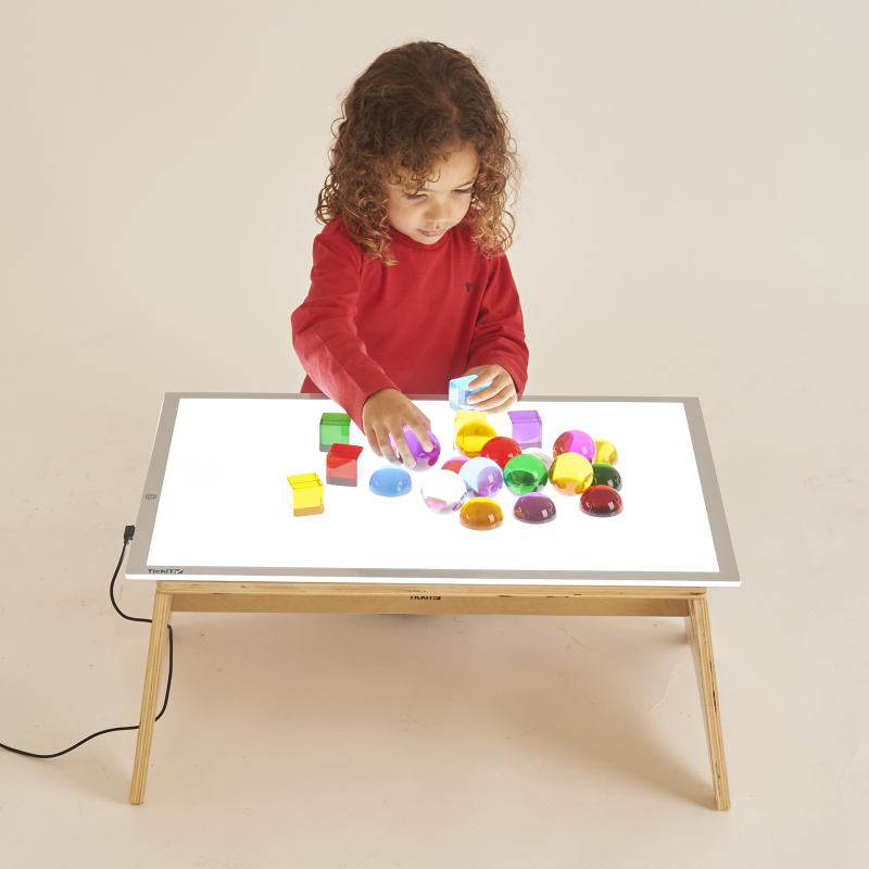 Child playing with colorful blocks on a light-up table against a beige background