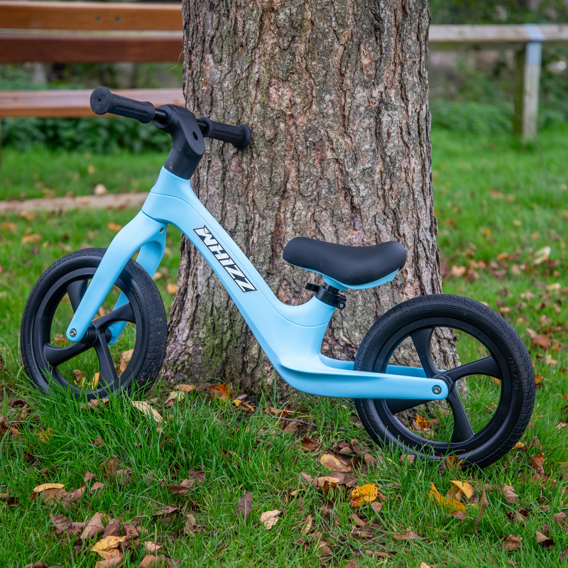 Blue balance bike leaning against a tree in a park setting