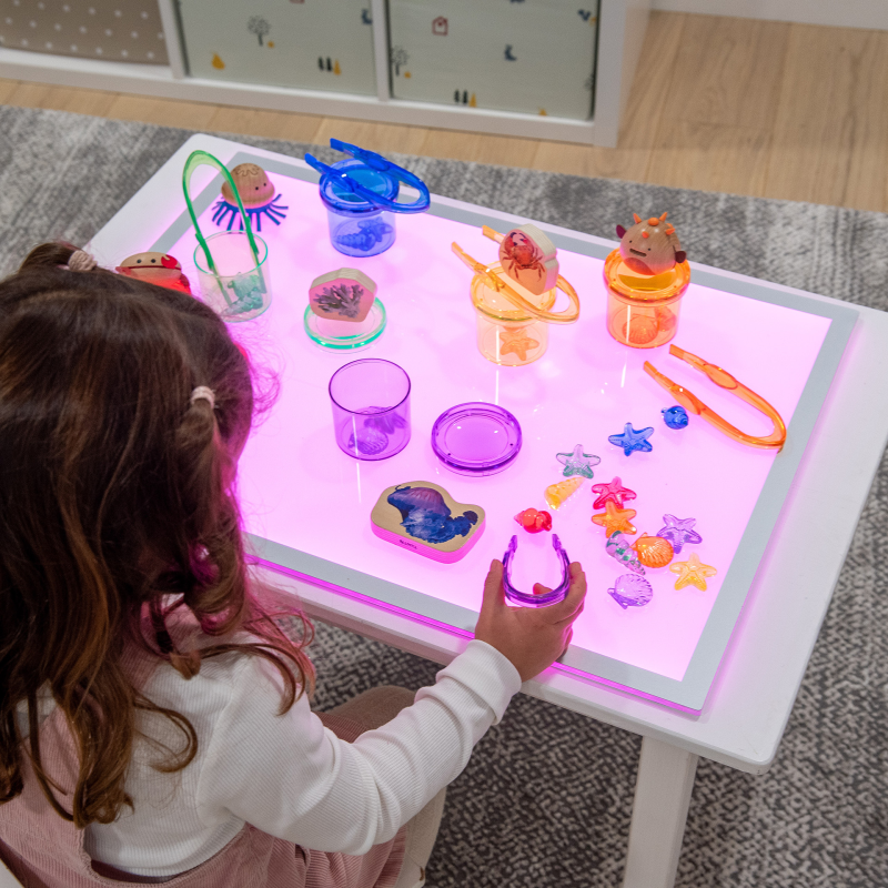 Child playing with toys on a light-up panel in a room.