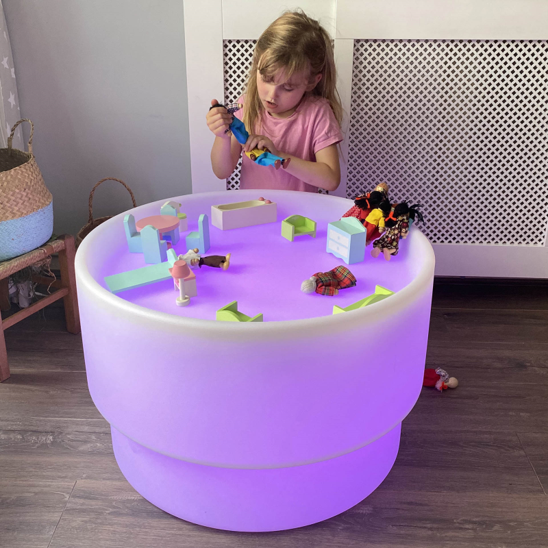 Child playing with toys on a colorful LED table in a room.