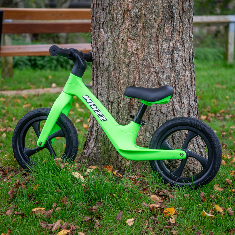 Green balance bike leaning against a tree in a park setting