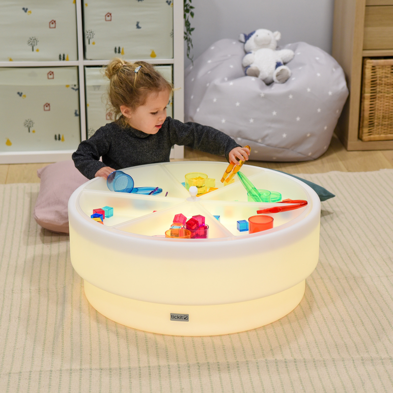 Child playing with toys on a illuminated round sensory table in a room.