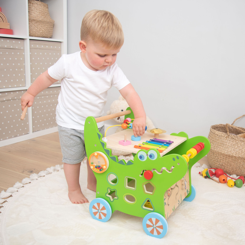 Child playing with a colorful toy walker in a room with shelves and baskets.