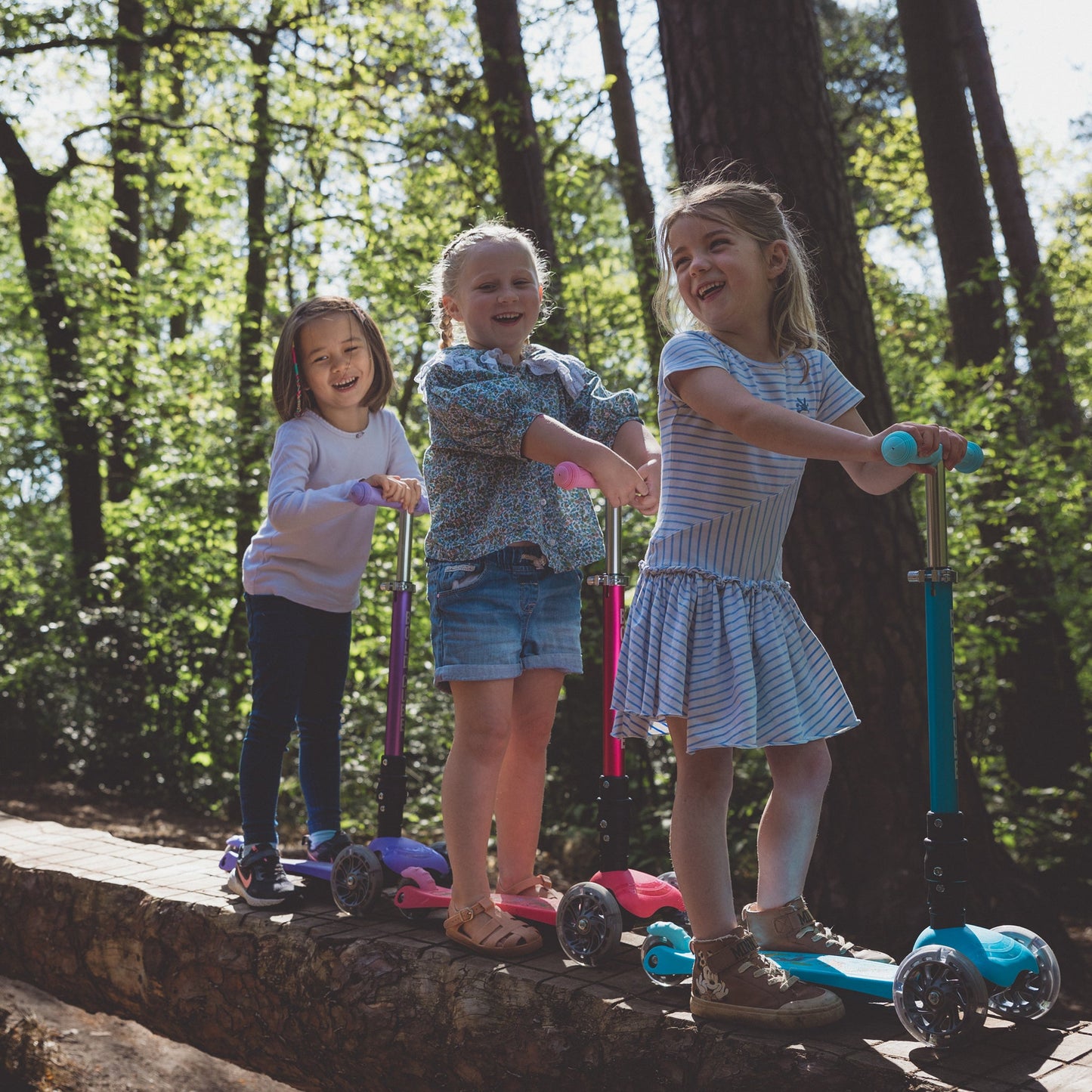 Three children on scooters in a forest setting