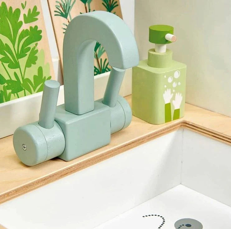 Children's toy faucet and sink set on a wooden surface with a floral-patterned wall in the background.