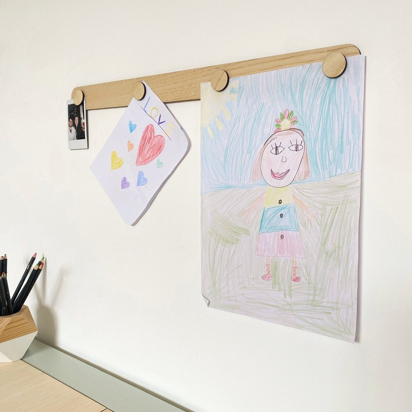 Children's drawings on a wooden frame against a white wall.