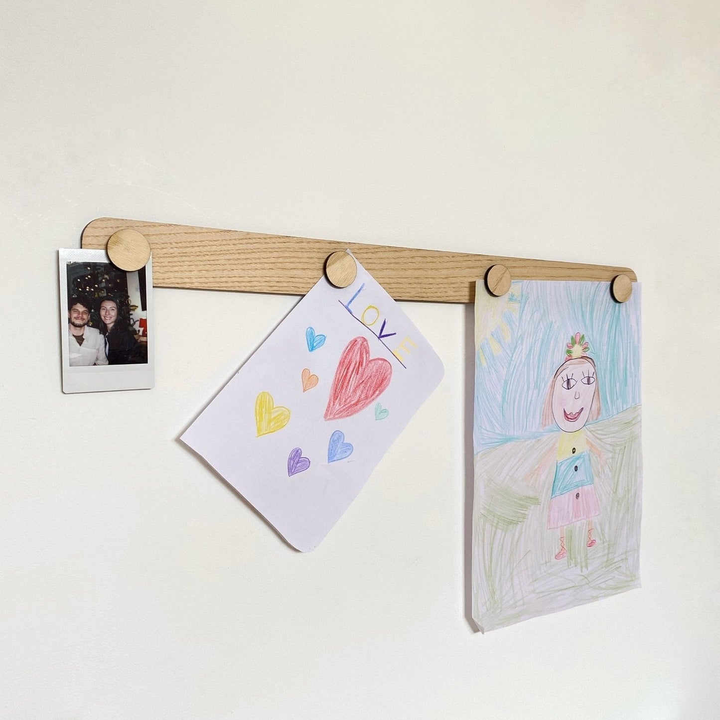 Wooden pegboard with children's drawings and a photo on a white wall.