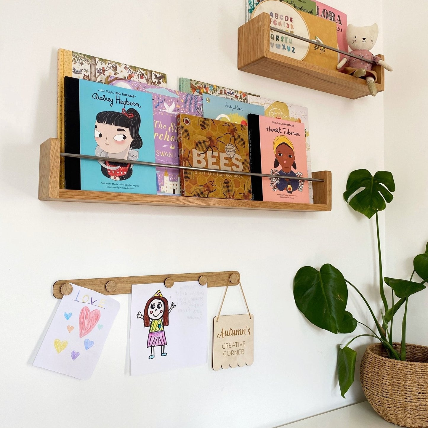Wooden shelves with children's books and drawings on a white wall.