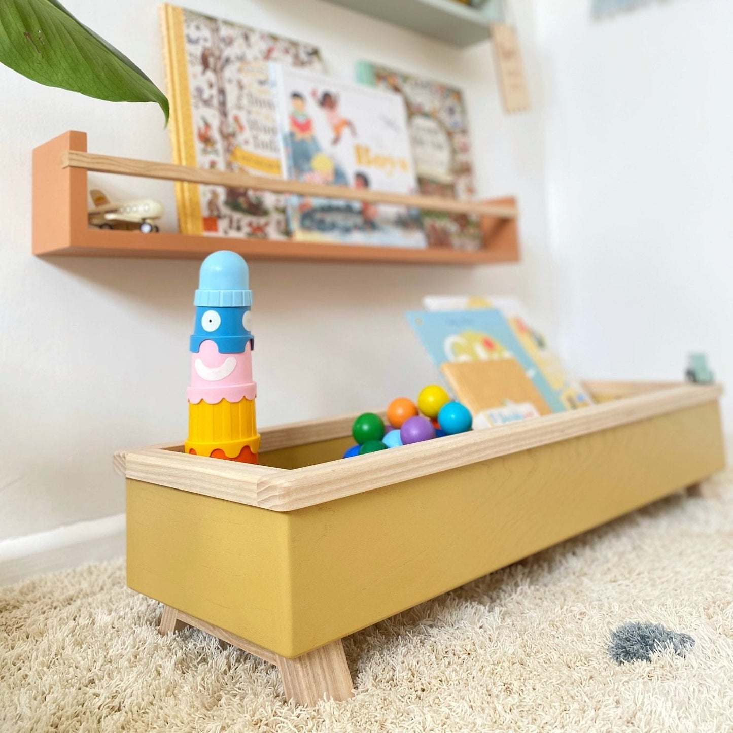 Children's play area with a yellow toy box, colorful toys, and shelves with books and decor.
