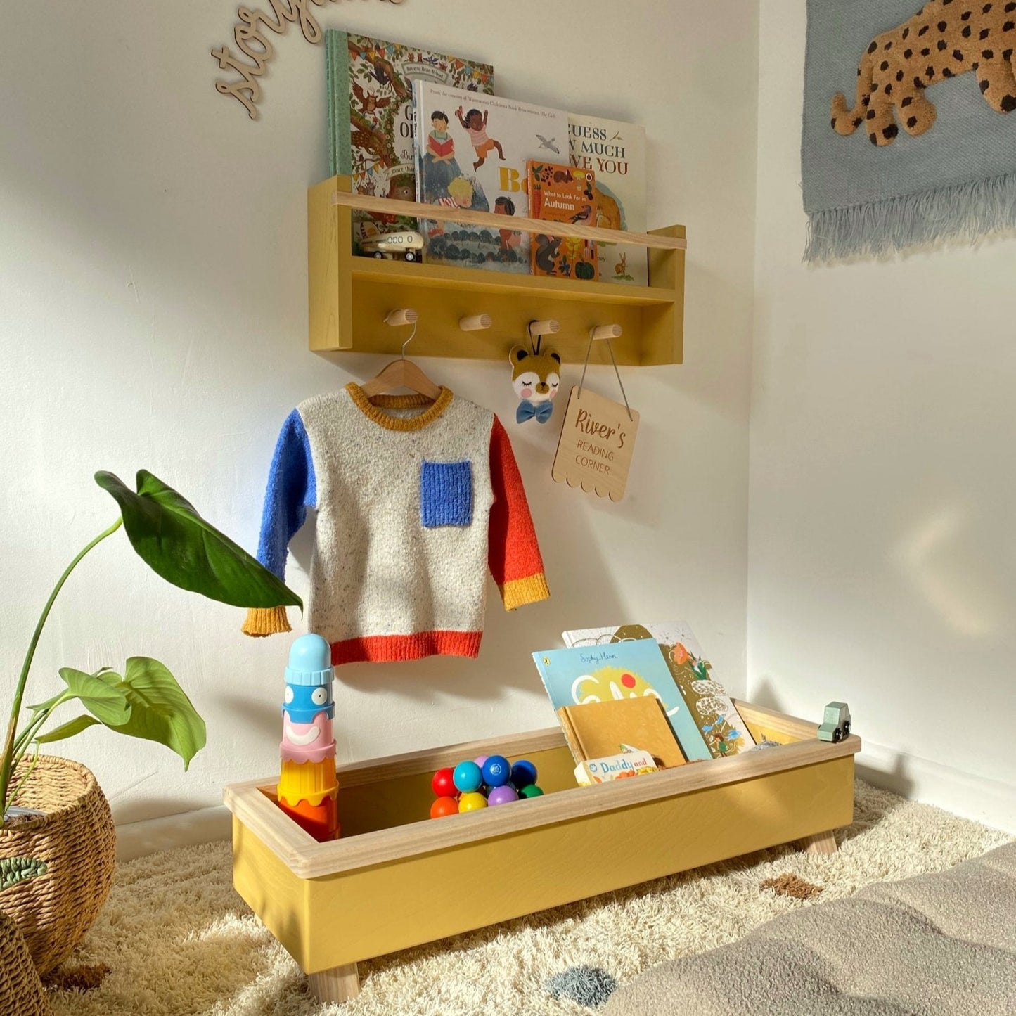 Children's play area with a wooden shelf, colorful sweater, and toys on a carpeted floor.