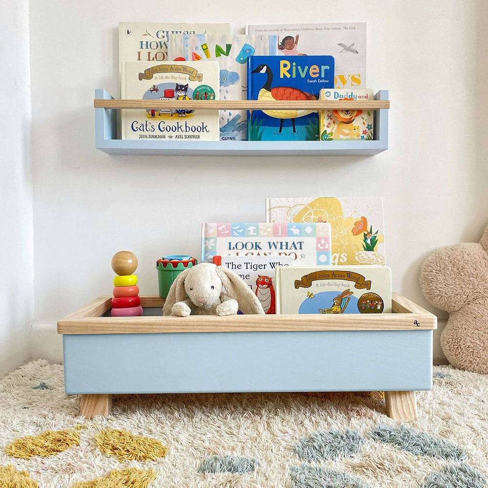 Children's toys and books on a shelf and tray against a white wall.