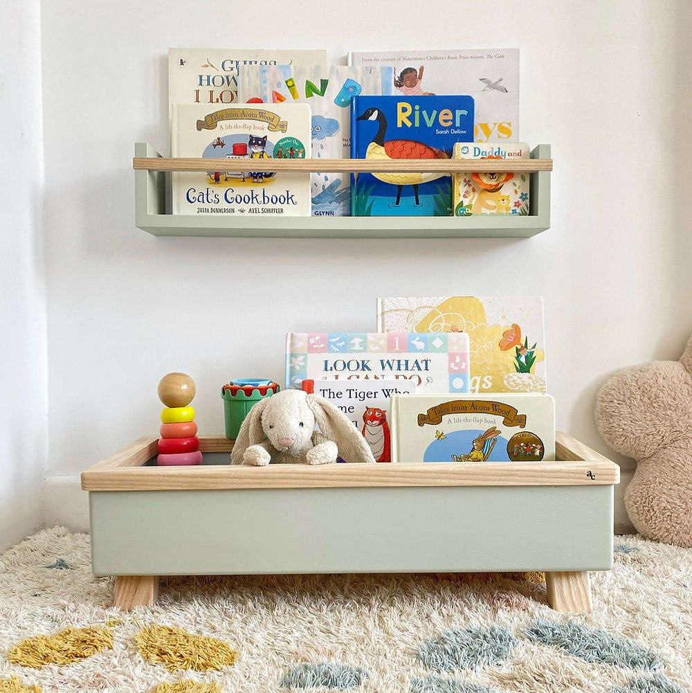 Green toy box with teddy bear, books, and abacus on a carpeted floor.