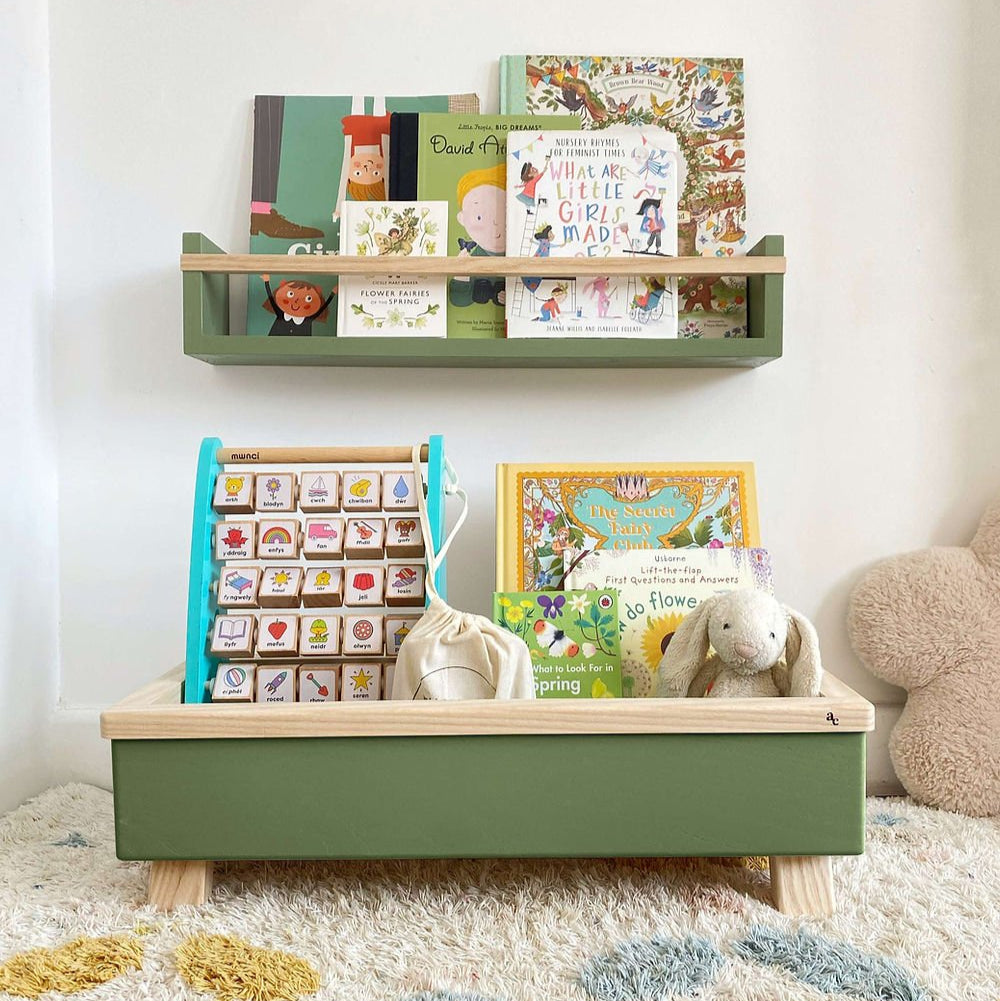 Children's room with a green shelf and storage unit displaying books and toys on a carpeted floor.