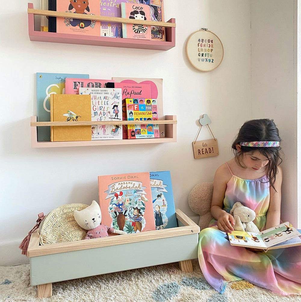 Child reading a book on the floor with colorful shelves displaying books in the background.