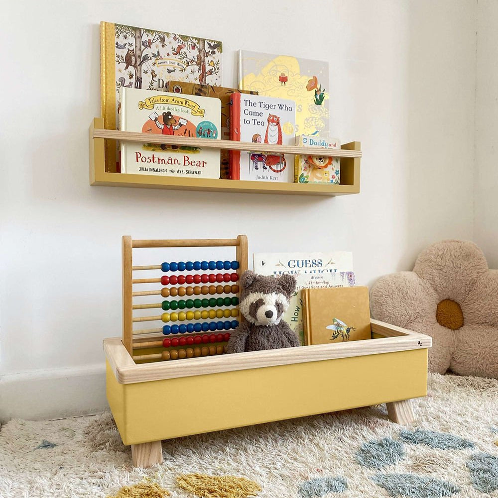 Yellow toy box with teddy bear, books, and abacus on a carpeted floor.