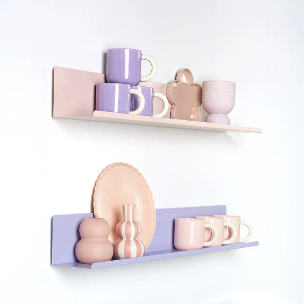 Decorative shelves with pastel-colored mugs, plates, and a vase on a white wall.
