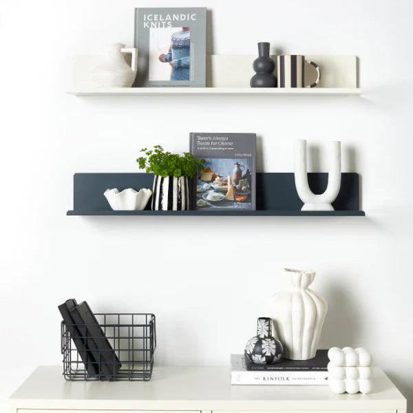 White wall with shelves displaying books, decor items, and a vase.
