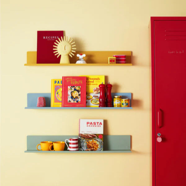 Shelves with cookbooks and kitchen items against a yellow wall with a red door.