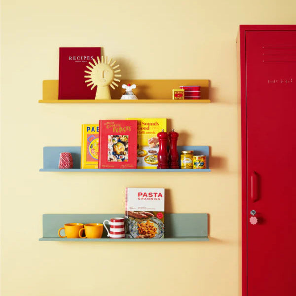 Shelves with cookbooks and kitchen items against a yellow wall with a red locker.