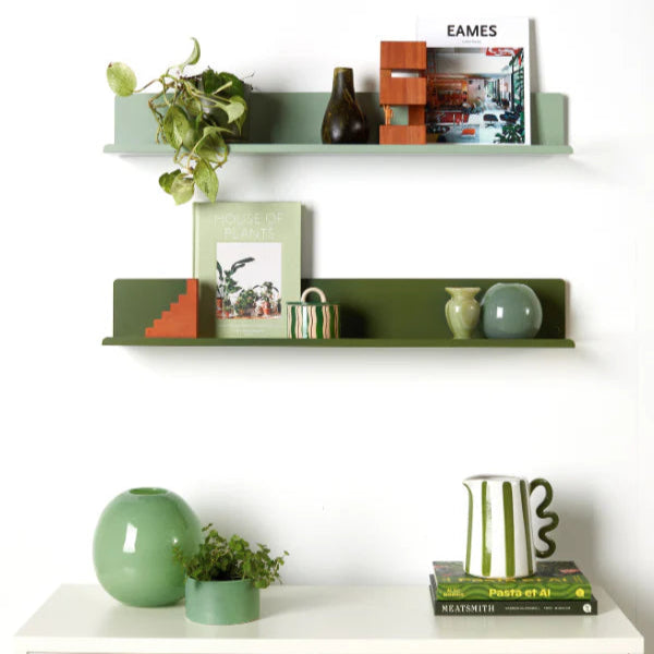 Decorative shelves with books, vases, and plants against a white wall.