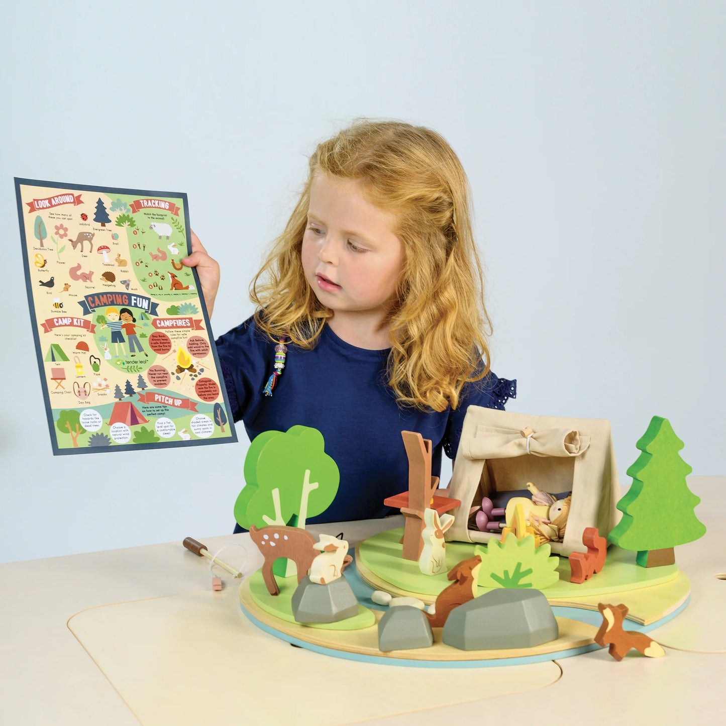 Child playing with a wooden forest scene toy set on a light blue background