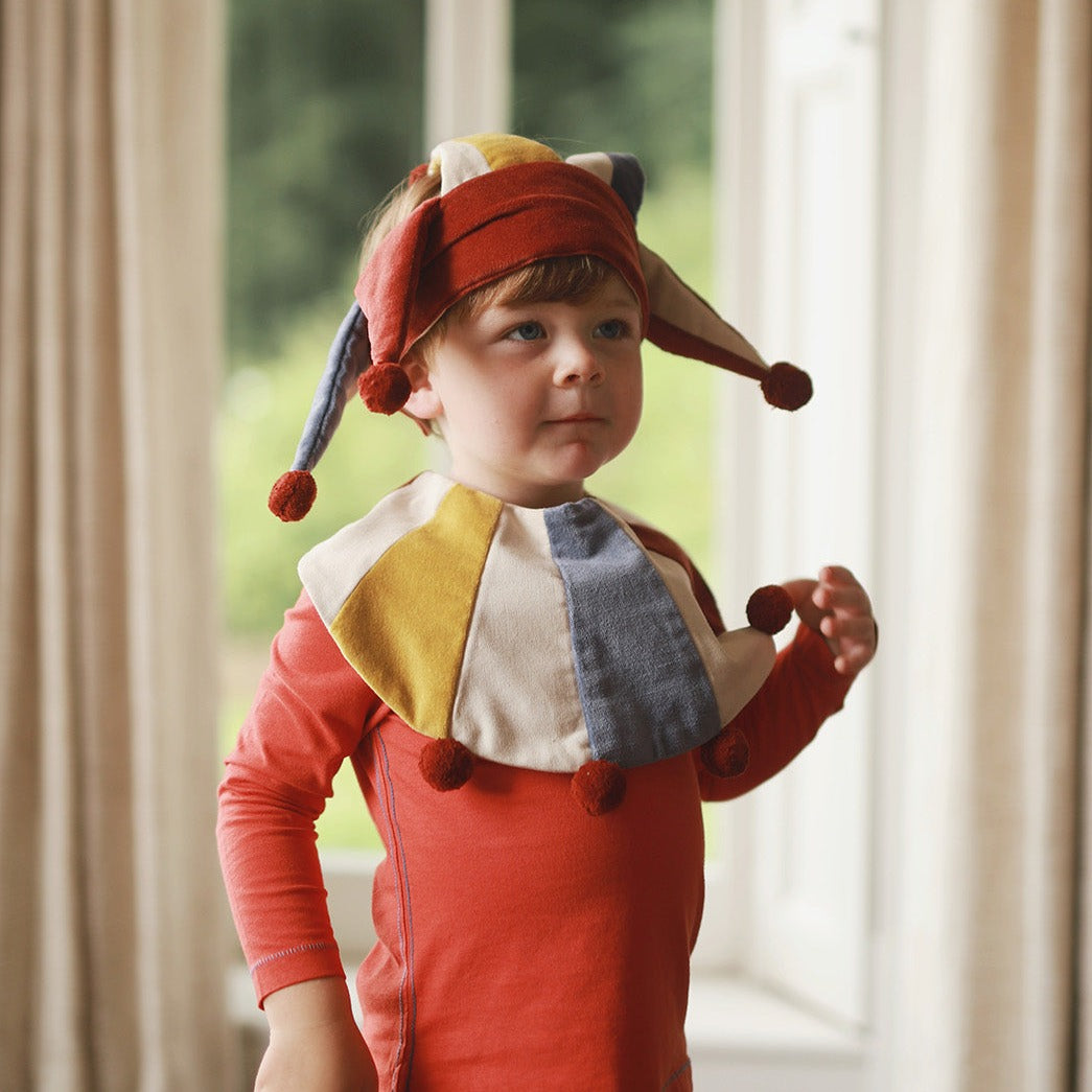 Child wearing a colorful costume with a red outfit and multicolored hat indoors.