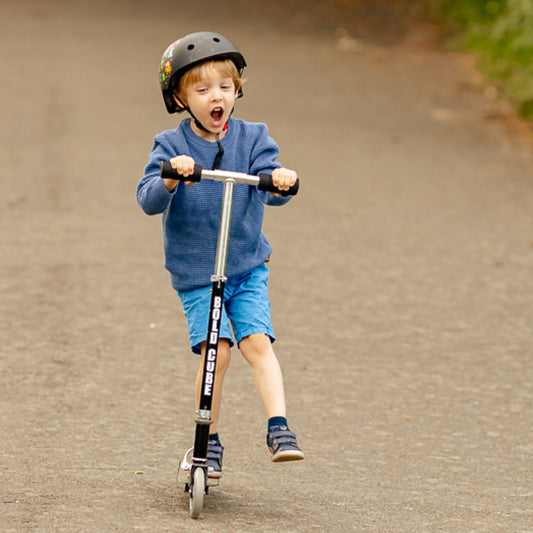 Child riding a scooter on a paved road wearing a helmet